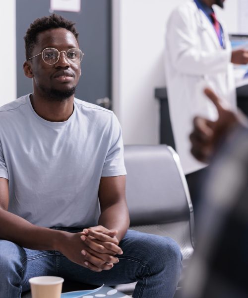 African american patients talking about healthcare and diagnosis in waiting room lobby at health center. Group of men sitting in area at hospital reception before attending checkup examination.
